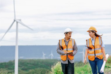 Erkek ve kadın mühendisler kırsal kesimdeki bir tepenin tepesinde ya da dağda rüzgar çiftliğinde çalışıyorlar. Yenilenebilir ve sürdürülebilir enerjinin gelecekteki üretimi için yenilikçi idealler.