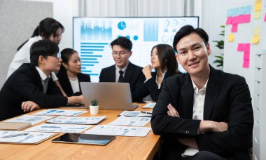 Focus portrait of successful confident male manager or executive in business wear with blurred background of businesspeople, colleagues working with financial report papers in office of harmony.