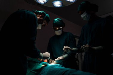 Steril ameliyathanedeki hastaya ameliyat yapan cerrahi ekip. Bir lambanın yaktığı ameliyathanede, profesyonel ve kendinden emin bir cerrahi ekip bilinçsiz bir hastaya tıbbi bakım sağlar..