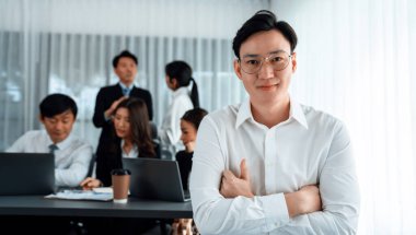 Portrait of focus young successful confident male manager, executive wearing business wear in harmony office arm crossed with blurred meeting background of colleagues, office worker.