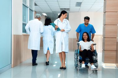 Doktor ve erkek hemşire, steril hastane koridorunda tekerlekli sandalyeli bir kadın hastayı naklediyor. Engelli hastalar için hastane konseptinde sağlık ve hemşirelik hizmeti.