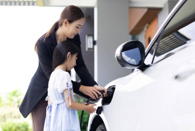 Evde şarj edilen elektrikli bir araçla okuldan yeni dönen anne ve kızın ilerici yaşam tarzı. Elektrikli araç, sürdürülebilir temiz enerjiyle çalışıyor..