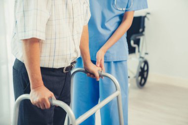 Physiotherapist assists her contented senior patient on folding walker. Recuperation for elderly, seniors care, nursing home.