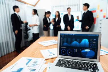 Focus laptop monitor display dashboard report by business intelligence, analyzed financial data for planning market strategy with blur background of standing office worker discussing in harmony office