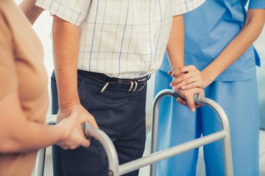 Contented senior man was helped on folding walking by his wife and caregiver. Recuperation for elderly, seniors care, nursing home.