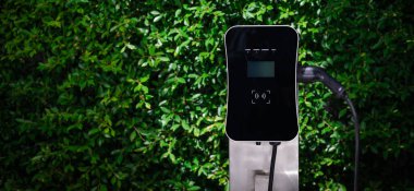 Charging station with greenery foliage background for combination of nature and alternative energy for progressive future renewable energy for electric car. Charger point with connecter device.