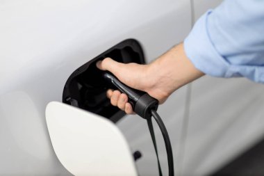 Closeup progressive man holding EV charger plug from public charging station for electric vehicle with background of residential building as concept eco-friendly sustainability energy car concept.