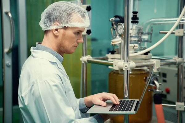 Cbd油抽出器の近くでラップトップを扱う薬局の科学者と 薬用大麻製品を作成するために使用される科学機械 — ストック写真