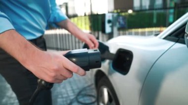 İlerici işadamı, şehir merkezinde dolaşmadan önce şarj cihazından elektrikli arabasına şarj prizi takıyor. Çevre dostu şarj edilebilir araba, sürdürülebilir ve temiz enerjiyle çalışıyor..