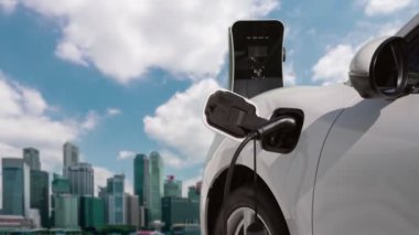 Elektrikli araç, EV araba şehir merkezindeki şarj istasyonunda şarj oluyor. Etrafı yüksek gökdelenlerle çevrili. Çevre dostu yenilikçi temiz enerji kavramı.