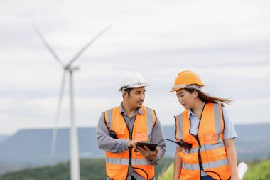 Erkek ve kadın mühendisler kırsal kesimdeki bir tepenin tepesinde ya da dağda rüzgar çiftliğinde çalışıyorlar. Yenilenebilir ve sürdürülebilir enerjinin gelecekteki üretimi için yenilikçi idealler.