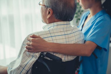 Rear view of a caregiver and her contented senior patient gazing out through the window. Elderly illness, nursing homes for the elderly, and pensioner life