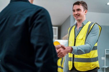 An engineer with a protective vest handshake with an investor in his office. Following a successful meeting, employee and employer form a partnership.