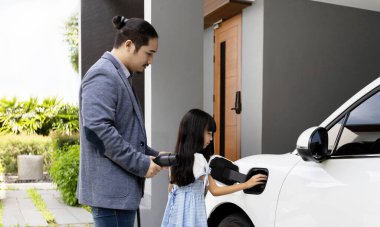 Progressive father and daughter plugs EV charger from home charging station to electric vehicle. Future eco-friendly car with EV cars powered by renewable source of clean energy.