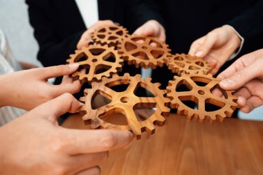 Closeup hand holding wooden gear by businesspeople wearing suit for harmony synergy in office workplace concept. Group of people hand making chain of gears into collective form for unity symbol.