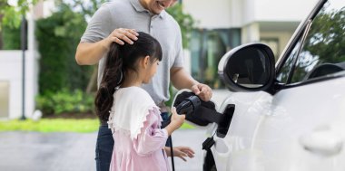 Progressive father and daughter returned from school in electric vehicle that is being charged at home. Electric vehicle driven by renewable clean energy. Home charging station concept for environment