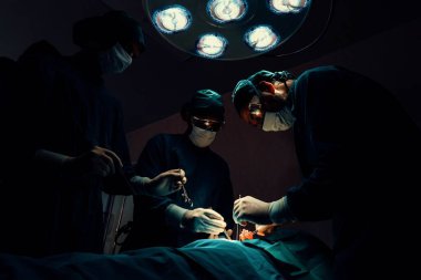 Steril ameliyathanedeki hastaya ameliyat yapan cerrahi ekip. Bir lambanın yaktığı ameliyathanede, profesyonel ve kendinden emin bir cerrahi ekip bilinçsiz bir hastaya tıbbi bakım sağlar..