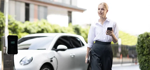 Businesswoman Using Tablet Walking While Recharging Her Electric Vehicle Charging —  Fotos de Stock