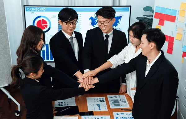 Closeup business team of suit-clad businessmen and women join hand stack together and form circle. Colleague collaborate and work together to promote harmony and teamwork concept in office workplace.