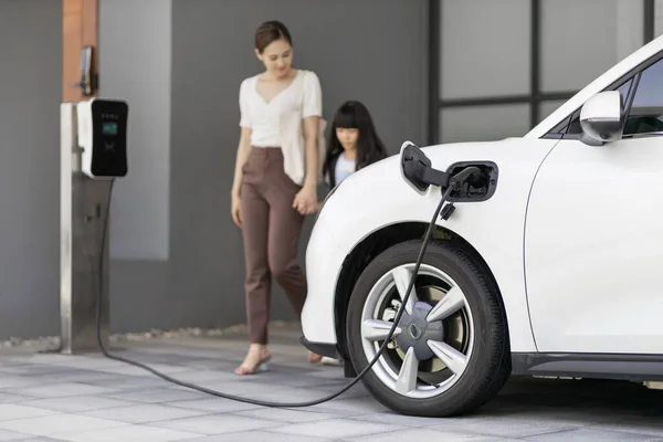 母亲和女儿的进步生活方式 他们刚从学校乘电动汽车回来 在家里充电 可持续清洁能源驱动的电动汽车 — 图库照片