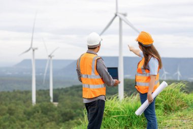Erkek ve kadın mühendisler kırsal kesimdeki bir tepenin tepesinde ya da dağda rüzgar çiftliğinde çalışıyorlar. Yenilenebilir ve sürdürülebilir enerjinin gelecekteki üretimi için yenilikçi idealler.
