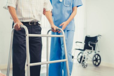 Physiotherapist assists her contented senior patient on folding walker. Recuperation for elderly, seniors care, nursing home.