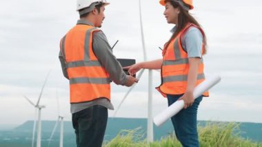 Erkek ve kadın mühendisler kırsal kesimdeki bir tepenin tepesinde ya da dağda rüzgar çiftliğinde çalışıyorlar. Yenilenebilir ve sürdürülebilir enerjinin gelecekteki üretimi için yenilikçi idealler.