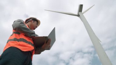 Gökyüzü arka planına sahip bir rüzgar türbini üzerinde çalışan mühendis. Yenilenebilir ve sürdürülebilir enerjinin gelecekteki üretimi için yenilikçi bir ideal. Rüzgar türbininden enerji üretimi.