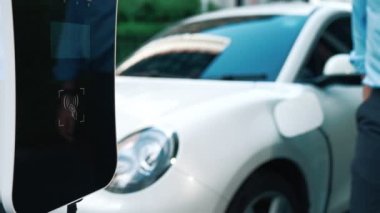 Bir adam kredi kartını, şarj istasyonundaki elektrikli aracının temiz ve sürdürülebilir enerjisini ödemek için kullanıyor. Yenilikçi adam şarj edilebilir aracına güç sağlamak için ödeme yapıyor..