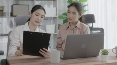 Ofis çalışma alanında birlikte çalışan iki genç hevesli iş kadını. Genç meslektaşlar tartışırken ve dizüstü bilgisayar kullanırken. Modern ofis çalışanları masada birlikte oturuyorlar..