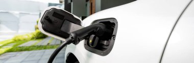 Closeup electric vehicle plugged-in with cable from charging point powered for progressive concept by alternative clean energy rechargeable EV car at home charging station.