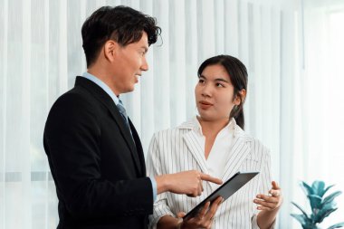Manager advising guiding younger colleague with tablet in workplace. Couple businesspeople in formal wear working together on financial strategy as concept of teamwork and harmony in office.