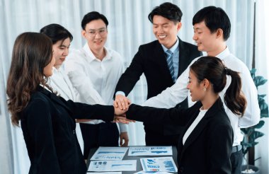 Closeup business team of suit-clad businessmen and women join hand stack together and form circle. Colleague collaborate and work together to promote harmony and teamwork concept in office workplace.