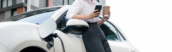 Focus Businessman Using Phone Leaning Electric Vehicle Holding Coffee Blurred — Stock fotografie