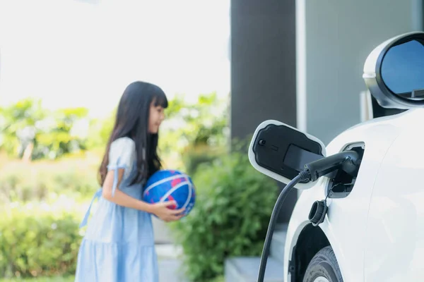 Focus home electric charging station for electric vehicle as alternative clean sustainable energy technology concept with blurred progressive young girl playing in the background at her home.