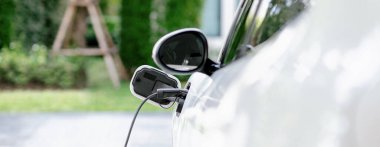 Closeup electric vehicle plugged-in with cable from charging point powered for progressive concept by alternative clean energy rechargeable EV car at home charging station.