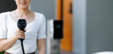 Çevre ve ekoloji için alternatif sürdürülebilir temiz ve yeşil enerji kavramı olarak kameraya elektrikli araç için EV prizi tutan yakın plan adamı.