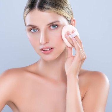 Alluring beautiful female model applying powder puff for facial makeup concept. Portrait of flawless perfect cosmetic skin woman put powder foundation on her face in isolated background.