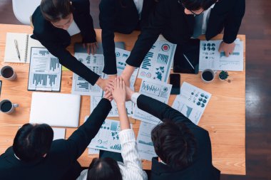Top view cohesive group of business people join hands together, form circle over table filled with financial report paper. Colleagues working to promote harmony and team building concept in workplace.