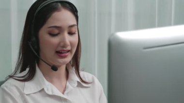 Masasında dizüstü bilgisayarla çalışan kulaklık ve mikrofon takan Asyalı müşteri destek operatörü. Hevesli kadın çalışanlar müşteri hizmetleri sunuyor, destekleyici çağrı merkezi temsilcisi müşterilere yardım ediyor.