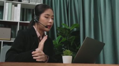 Kulaklık ve mikrofon takan iş kadını masasında çalışıyor ve dizüstü bilgisayar kullanıyor. Uzaktan kumandalı online toplantı için dizüstü bilgisayar kullanan hevesli kadın çalışanlar, ofiste iş videosu konferansı.
