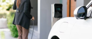 İlerici kadın elektrikli arabasının fişini şarj istasyonuna takıyor. İlerici bir yaşam tarzında elektrikli araç kullanımı kavramı temiz çevreye katkıda bulunur.