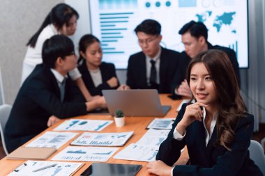 Focus portrait of female manger, businesswoman in the harmony meeting room with blurred of colleagues working together, analyzing financial paper report and dashboard data on screen in background.