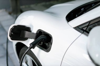 Closeup electric vehicle plugged-in with cable from charging point powered for progressive concept by alternative clean energy rechargeable EV car at home charging station.