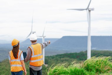 Erkek ve kadın mühendisler kırsal kesimdeki bir tepenin tepesinde ya da dağda rüzgar çiftliğinde çalışıyorlar. Yenilenebilir ve sürdürülebilir enerjinin gelecekteki üretimi için yenilikçi idealler.