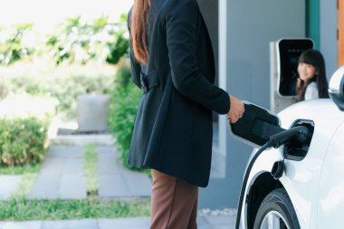 Evde şarj edilen elektrikli bir araçla okuldan yeni dönen anne ve kızın ilerici yaşam tarzı. Elektrikli araç, sürdürülebilir temiz enerjiyle çalışıyor..