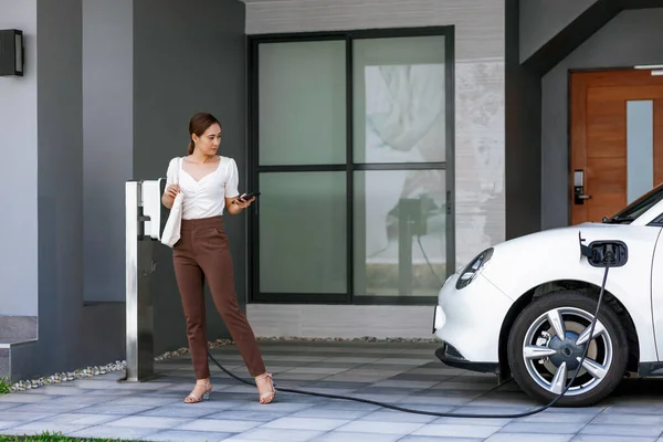 Progressive Asian Woman Holding Smartphone Electric Car Home Charging Station — Foto Stock