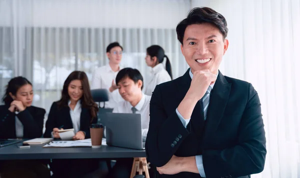 stock image Portrait of focus young successful confident male manager, executive wearing business wear in harmony office arm crossed with blurred meeting background of colleagues, office worker.