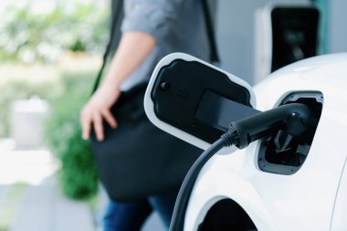 Focus electric car charging at home charging station with blurred progressive man walking in the background. Electric car using renewable clean for eco-friendly concept.