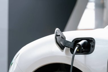 Closeup electric vehicle plugged-in with cable from charging point powered for progressive concept by alternative clean energy rechargeable EV car at home charging station.